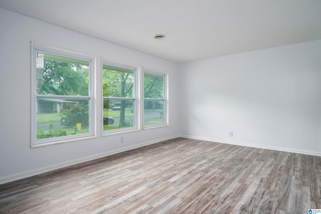 spare room featuring a wealth of natural light, wood finished floors, visible vents, and baseboards