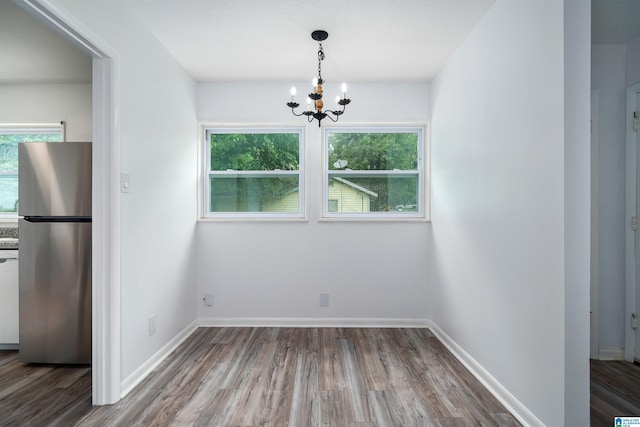 unfurnished dining area with baseboards, wood finished floors, and a notable chandelier