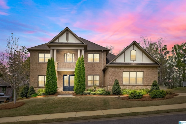 view of front of house with a lawn, brick siding, french doors, and stone siding