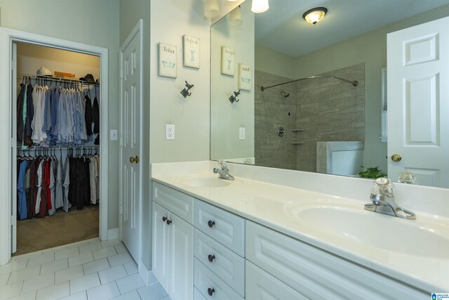 full bath featuring double vanity, tiled shower, a sink, and tile patterned flooring