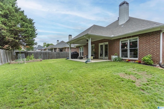 rear view of house with roof with shingles, brick siding, a fenced backyard, a patio, and a yard