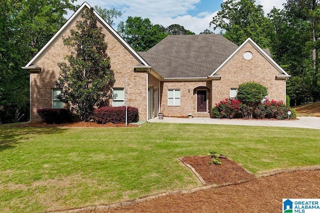 view of front of property featuring a shingled roof, a front lawn, and brick siding
