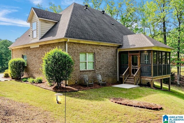 rear view of house featuring a sunroom, a shingled roof, a lawn, and brick siding