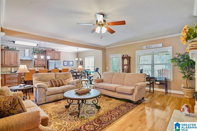 living room with light wood-type flooring, ornamental molding, ceiling fan with notable chandelier, and a wealth of natural light