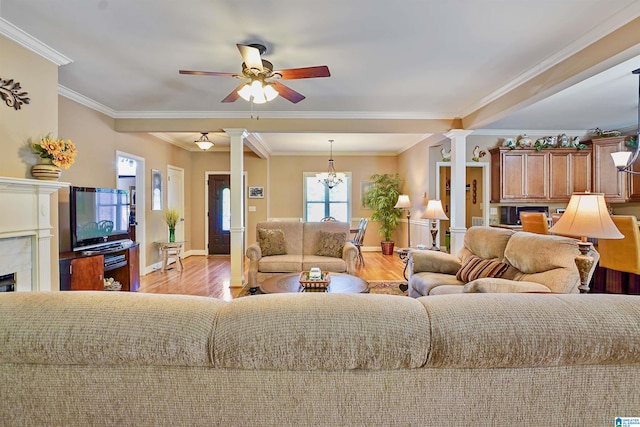 living area featuring light wood-style flooring, ceiling fan with notable chandelier, baseboards, decorative columns, and ornamental molding