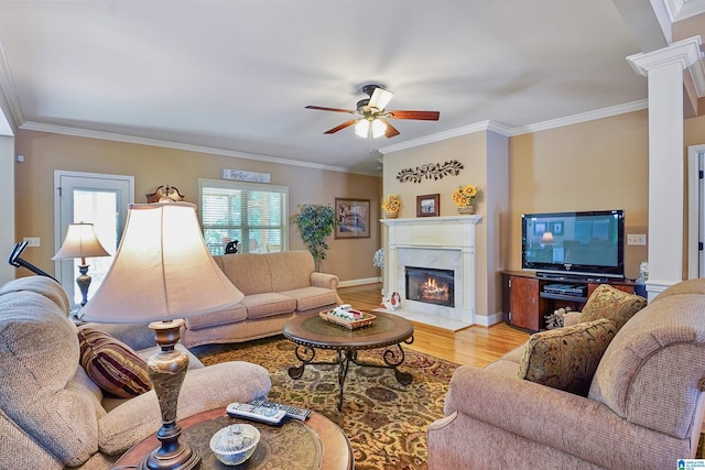 living area with crown molding, a fireplace, light wood-style floors, a ceiling fan, and decorative columns