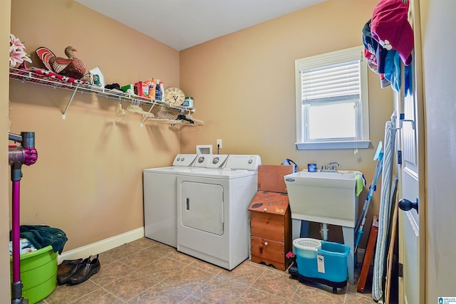 clothes washing area featuring washing machine and clothes dryer, laundry area, a sink, tile patterned flooring, and baseboards