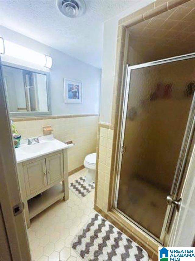 full bath featuring vanity, a shower stall, tile patterned flooring, and tile walls