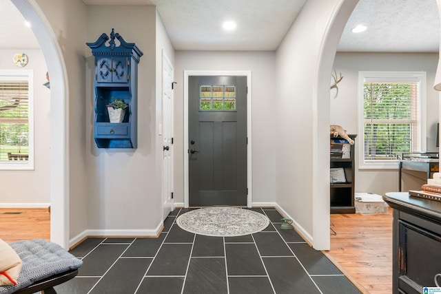 foyer featuring recessed lighting, arched walkways, dark tile patterned floors, and baseboards