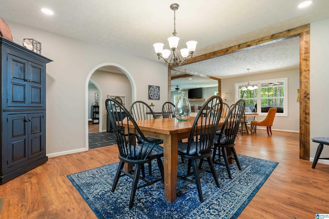 dining room with a chandelier, light wood-type flooring, baseboards, and arched walkways
