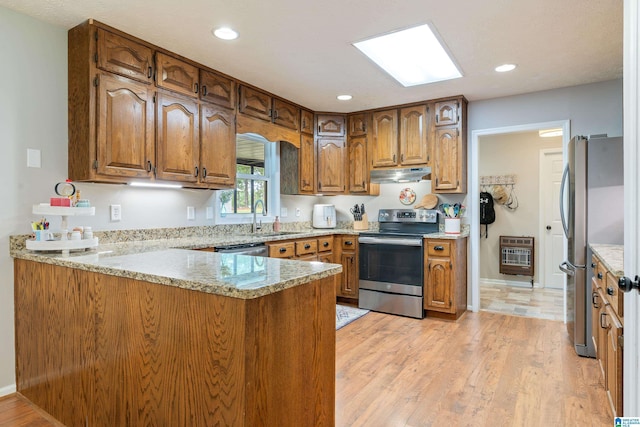 kitchen with heating unit, brown cabinetry, under cabinet range hood, appliances with stainless steel finishes, and a peninsula