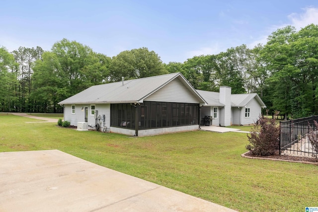 rear view of property with metal roof, a sunroom, and a lawn