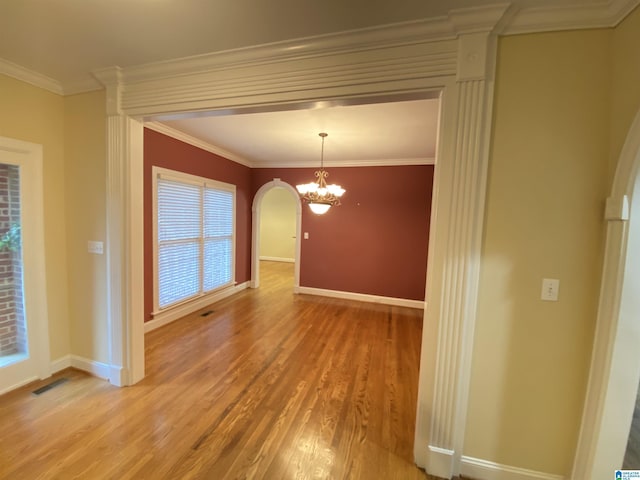 unfurnished room with baseboards, arched walkways, a notable chandelier, and wood finished floors