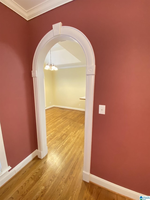 corridor featuring a notable chandelier, baseboards, ornamental molding, arched walkways, and wood finished floors