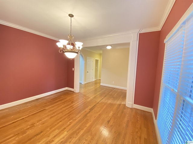 spare room featuring crown molding, light wood-style floors, a chandelier, arched walkways, and baseboards