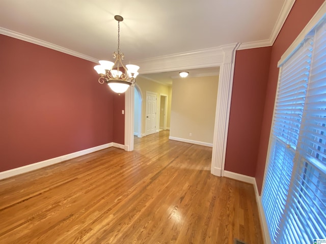 spare room featuring a chandelier, crown molding, baseboards, arched walkways, and wood finished floors