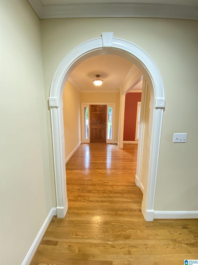 hallway featuring baseboards, light wood-type flooring, arched walkways, and crown molding
