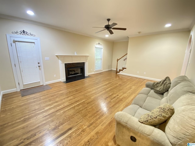 living room with light wood finished floors, a ceiling fan, stairs, baseboards, and ornamental molding