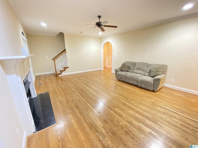 living area featuring light wood-style flooring, arched walkways, ceiling fan, and a fireplace