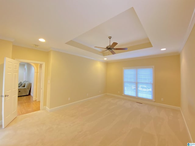empty room with a raised ceiling, ceiling fan, light carpet, and baseboards