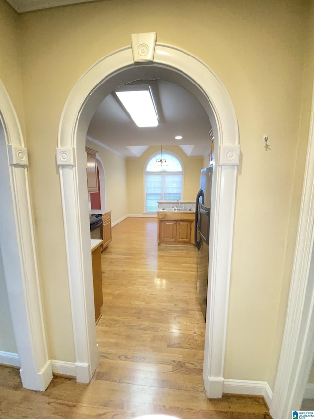 corridor with a sink, baseboards, light wood-style flooring, and arched walkways