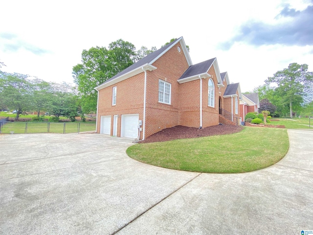 view of property exterior with a yard, brick siding, fence, a garage, and driveway