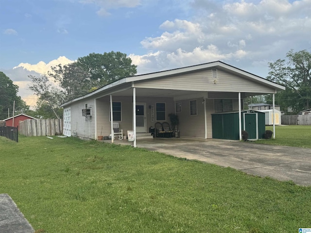 back of property featuring a lawn, fence, concrete driveway, and a storage shed