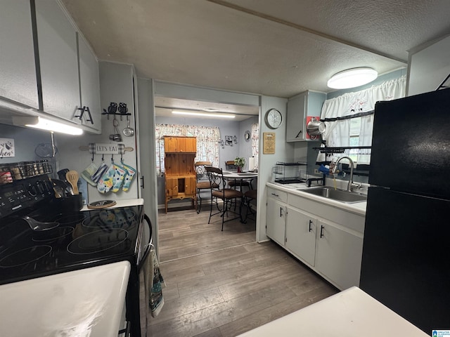 kitchen with a sink, light wood-type flooring, black appliances, light countertops, and a textured ceiling