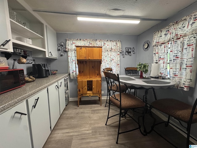 kitchen featuring a textured ceiling, open shelves, white cabinets, light countertops, and light wood-type flooring
