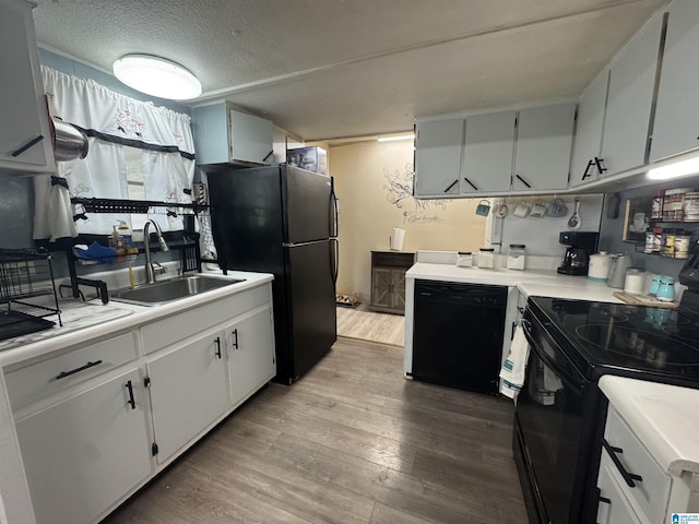 kitchen featuring black appliances, wood finished floors, light countertops, and a sink