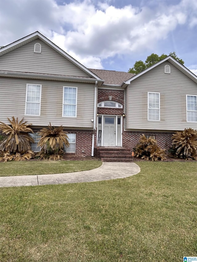 view of front of home with brick siding, entry steps, a shingled roof, and a front yard