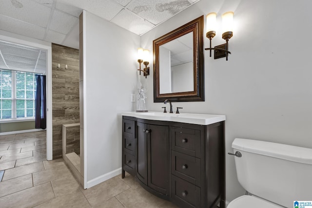 bathroom with a tile shower, toilet, vanity, baseboards, and a paneled ceiling