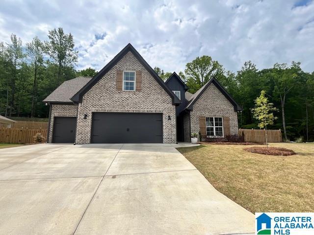 view of front of house with brick siding, fence, driveway, a front lawn, and an attached garage