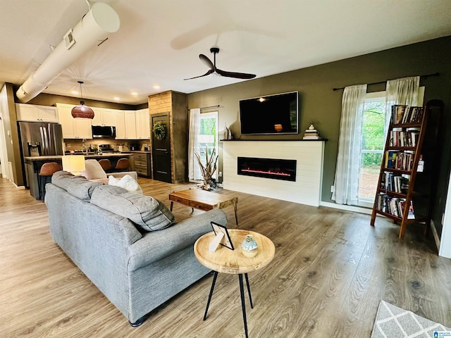 living room with a wealth of natural light, light wood-type flooring, a ceiling fan, and a glass covered fireplace