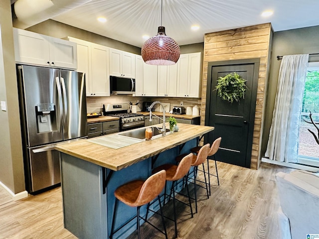 kitchen featuring a sink, stainless steel appliances, light wood-style flooring, wooden counters, and white cabinets
