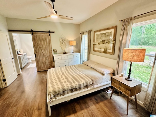 bedroom with wood finished floors, connected bathroom, a ceiling fan, and a barn door