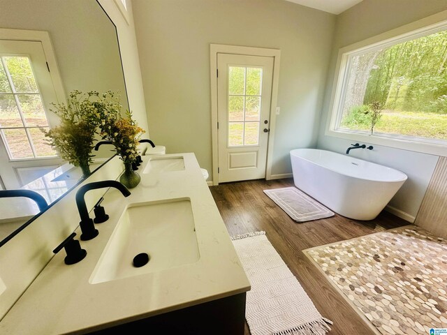 full bath with double vanity, wood finished floors, a freestanding bath, and a sink