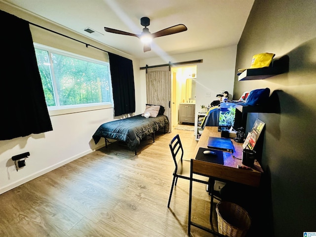 bedroom featuring a barn door, light wood-style floors, baseboards, visible vents, and a ceiling fan
