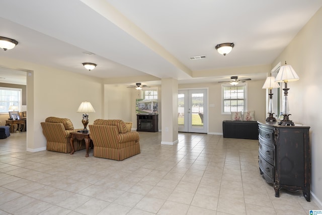living area featuring light tile patterned flooring, ceiling fan, visible vents, and baseboards