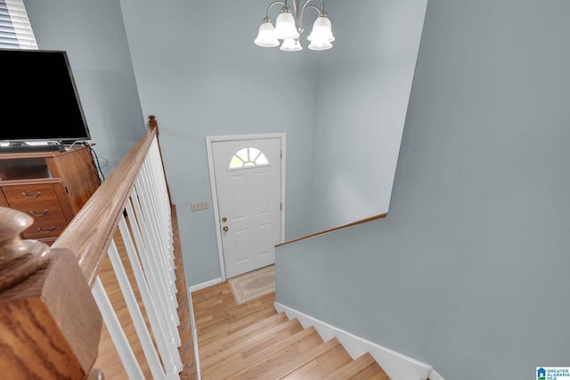 staircase with baseboards, wood finished floors, and a notable chandelier