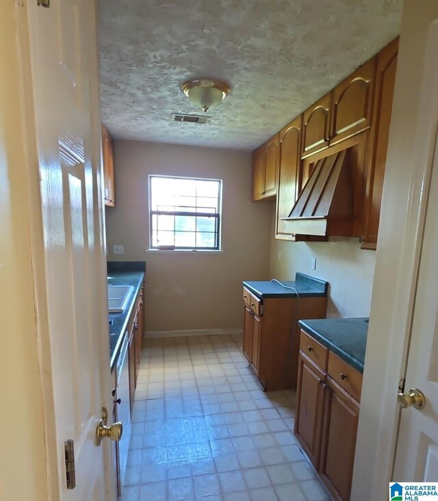 kitchen with a sink, brown cabinetry, visible vents, dark countertops, and light floors