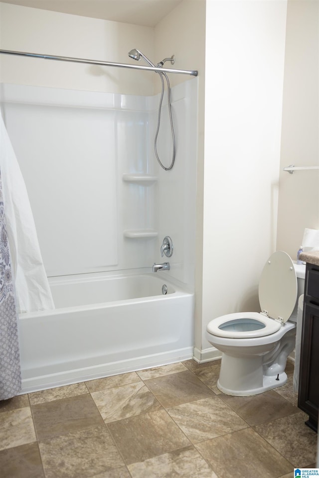 bathroom with vanity, shower / bath combination with curtain, toilet, stone finish floors, and baseboards