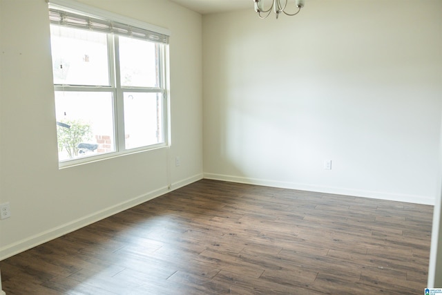 empty room with a chandelier, dark wood finished floors, and baseboards