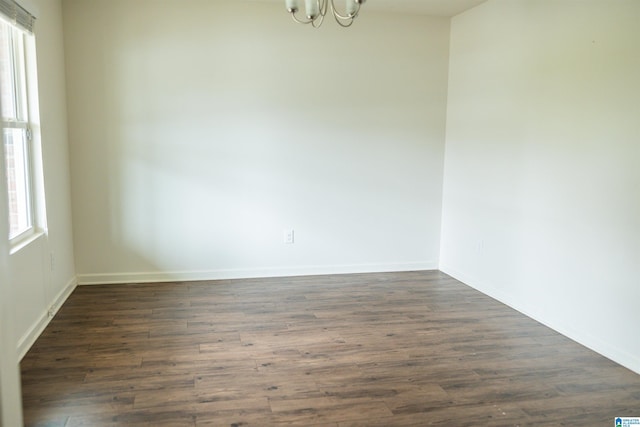 empty room featuring a chandelier, plenty of natural light, and dark wood-type flooring