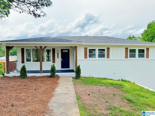 view of front of house featuring a shingled roof, board and batten siding, a porch, and brick siding