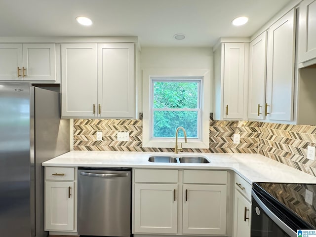 kitchen with appliances with stainless steel finishes, a sink, light countertops, white cabinetry, and backsplash