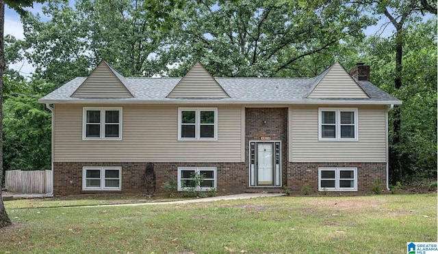 bi-level home featuring a chimney, brick siding, a front lawn, and roof with shingles