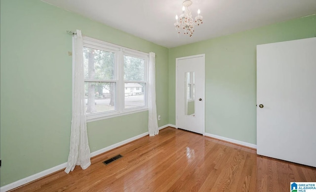 interior space with an inviting chandelier, wood finished floors, visible vents, and baseboards