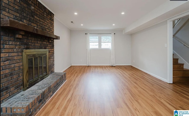 unfurnished living room featuring a brick fireplace, stairs, wood finished floors, and baseboards