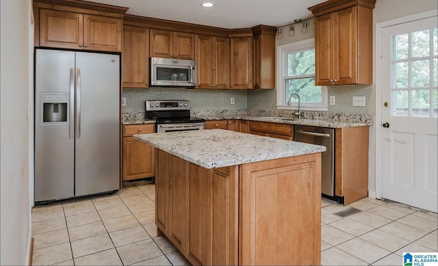 kitchen featuring a sink, light tile patterned floors, brown cabinetry, light stone counters, and appliances with stainless steel finishes